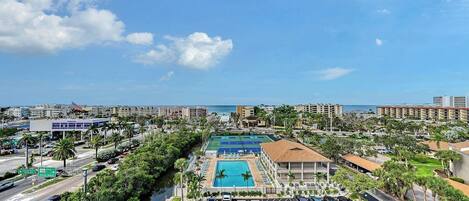 A resort with a swimming pool, tennis courts, and a view of the ocean.