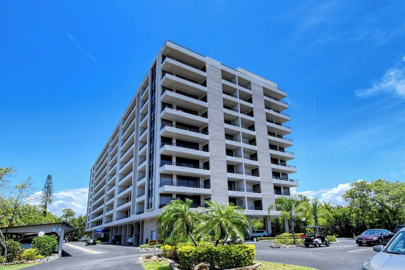 A multi-story hotel with a modern design, featuring balconies on each floor and a parking area in front.