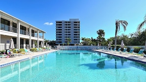 Una piscina con sillones de descanso, un edificio con balcones y palmeras.