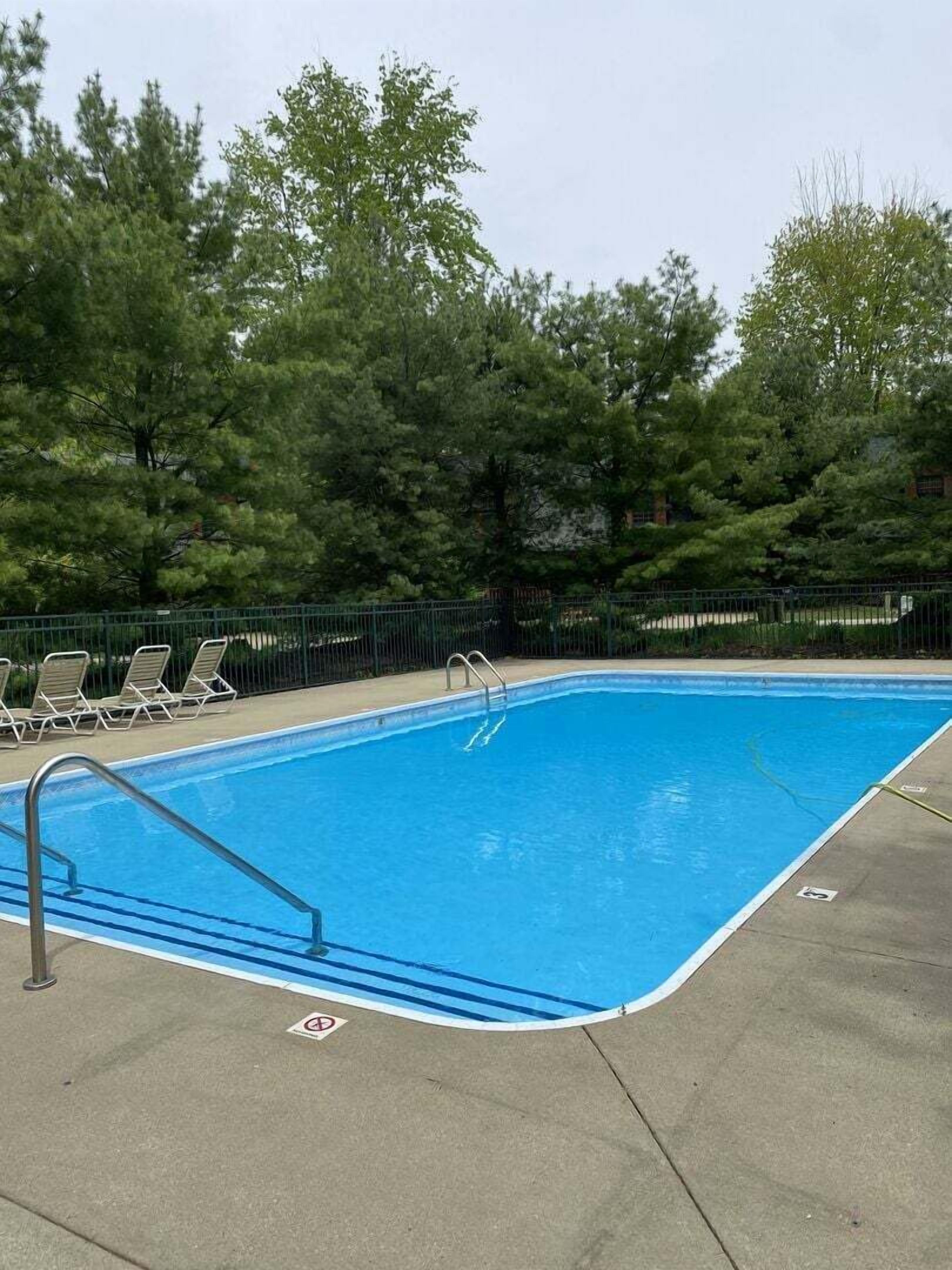 A rectangular swimming pool with a metal ladder, surrounded by a concrete deck.