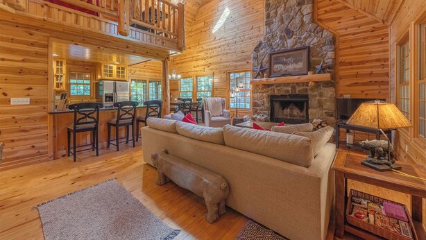 A log cabin interior with a cozy living area, a stone fireplace, and a kitchen with wooden cabinets.