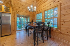 Un interior de madera con una mesa de comedor, sillas, una araña y ventanas grandes.