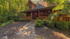 A log cabin with a stone pathway leading to the entrance, surrounded by dense greenery.