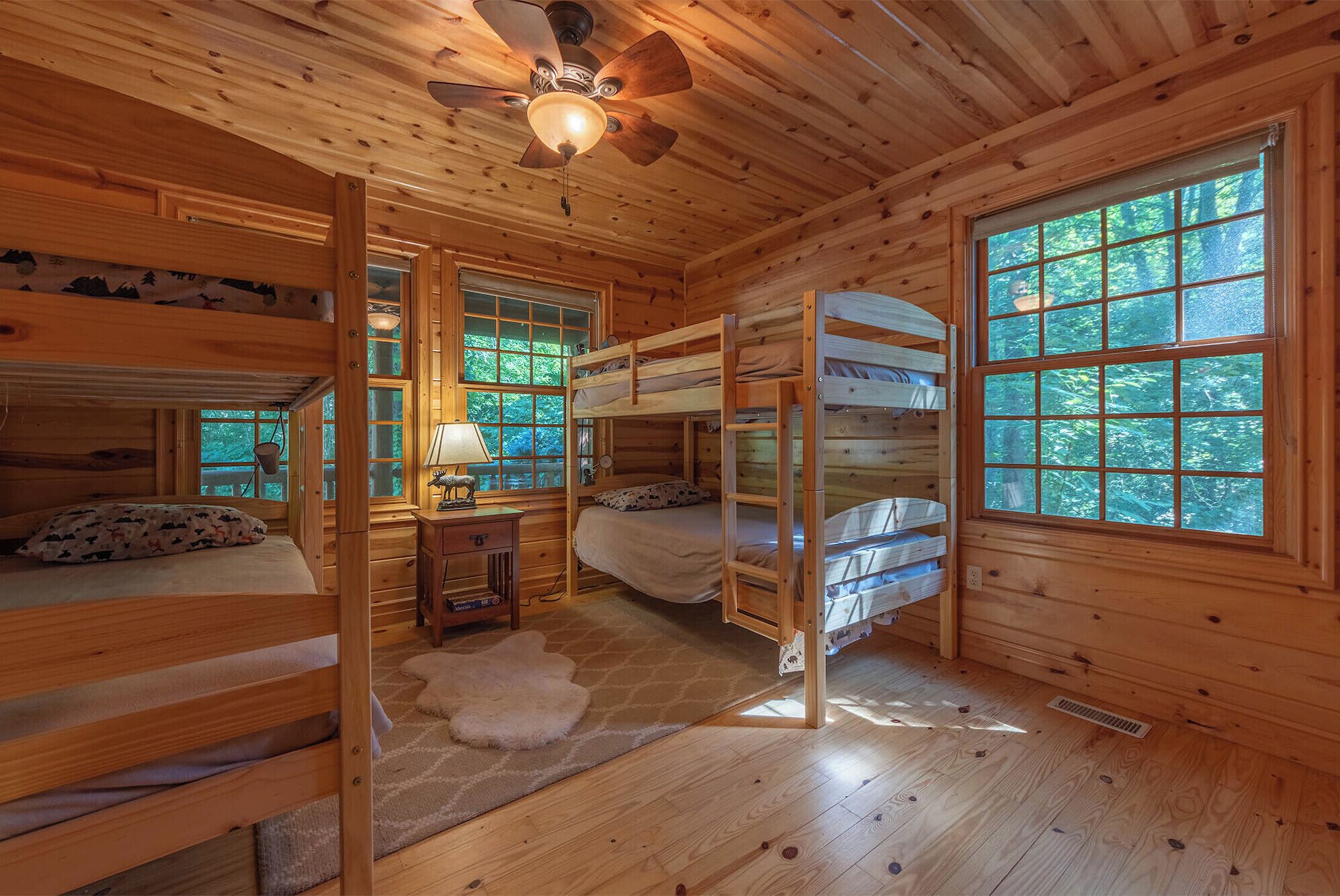 A cabin with wooden walls, bunk beds, a ceiling fan, and large windows.