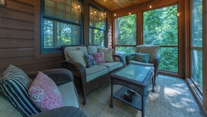 A covered porch with wicker furniture, large windows, and a wooden ceiling.