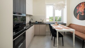 A modern kitchen with a built-in oven, a dining table with black chairs, and a white bench. - Warsaw Dream Apartment (Warszawa)