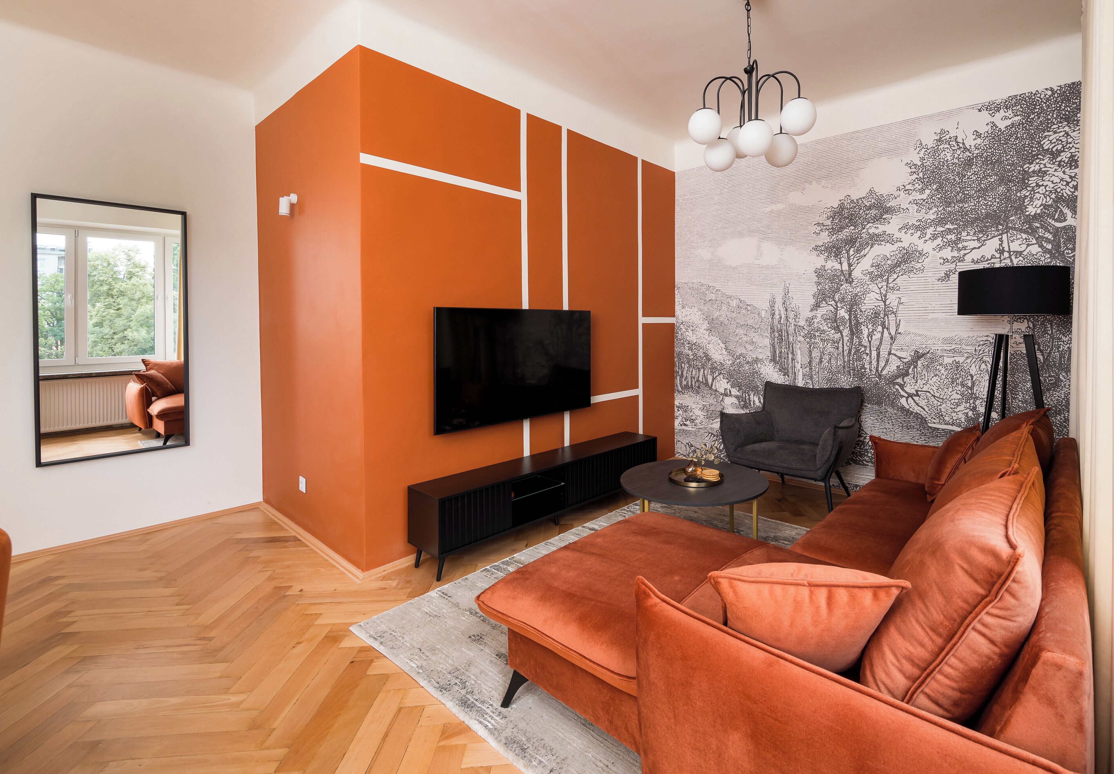 A modern living room with a large orange accent wall, a flat-screen TV, a sofa, a coffee table, and a patterned wall mural.