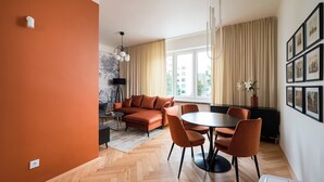 A modern living room with a herringbone floor, orange walls, a black sofa, a dining table with chairs, and a large window with curtains. - Warsaw Dream Apartment (Warszawa)