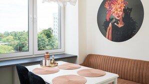 A room with a white table, a brown sofa, and a window with a view of greenery and buildings. - Warsaw Dream Apartment (Warszawa)
