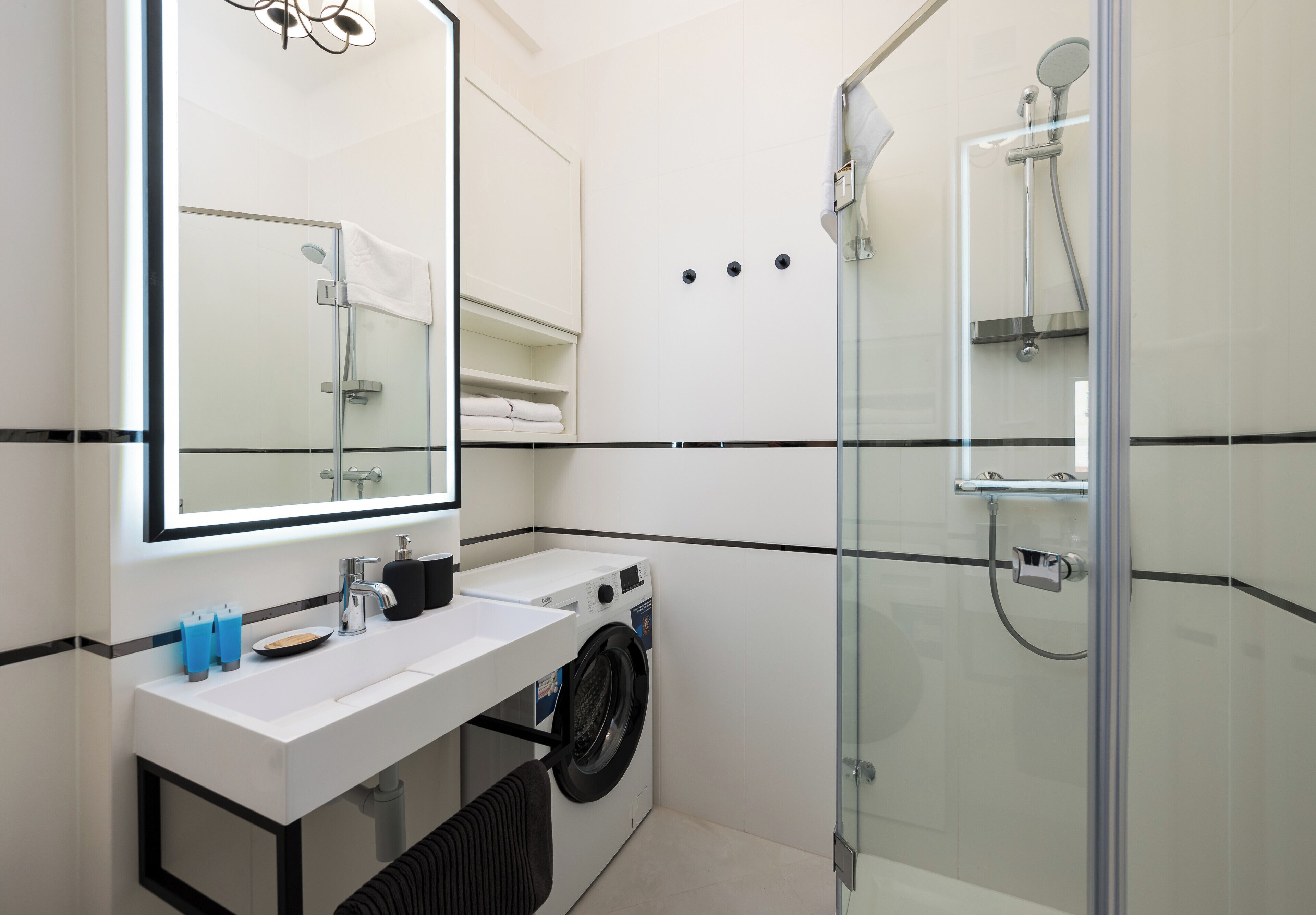 Un baño moderno con ducha acristalada, lavadora integrada y un espejo grande sobre el lavabo.