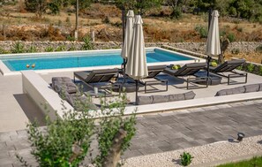 Ein Poolbereich mit Liegestühlen und Sonnenschirmen, umgeben von einer Steinmauer und viel Grün.