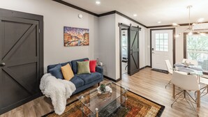 A modern living room with a blue sofa, a glass coffee table, and a painting on the wall. - Modern Casita w/Outdoor Tub- Unit B (Madison)