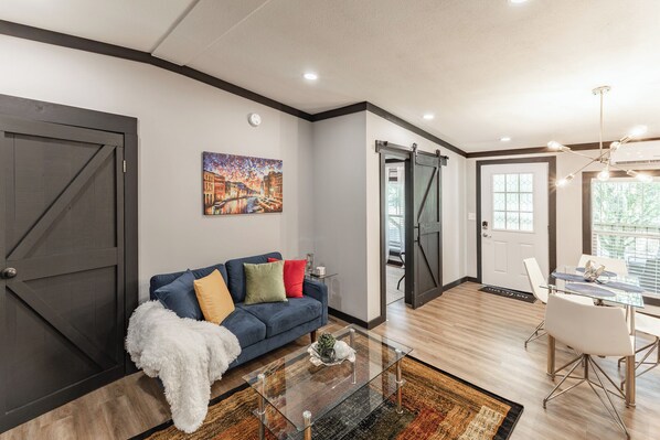 A modern living room with a blue sofa, a glass coffee table, and a painting on the wall.
