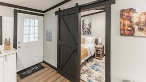 A bedroom with a bed, a nightstand, a wall-mounted lamp, and a door with a sliding barn door. - Modern Casita w/Outdoor Tub- Unit B (Madison)