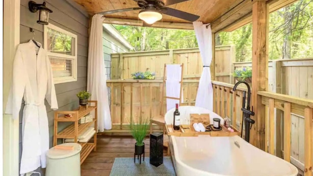 A wooden cabin bathroom with a bathtub, a ceiling fan, and a window overlooking greenery. - Modern Casita w/Outdoor Tub- Unit B (Madison)