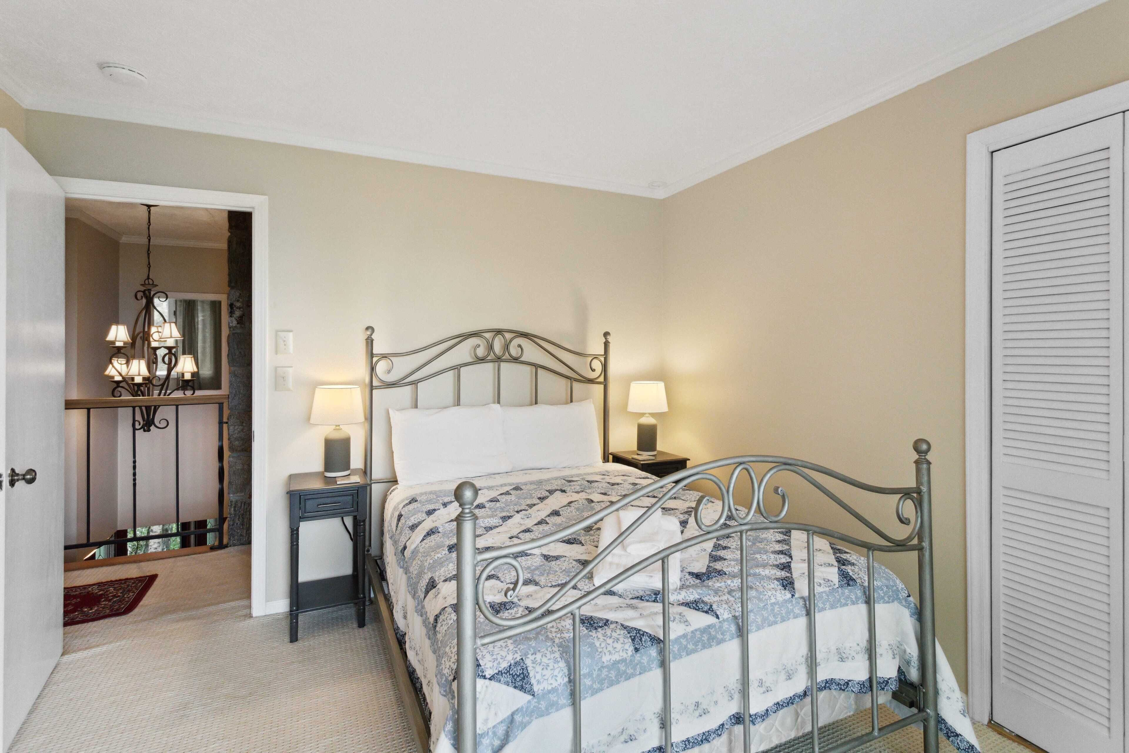 A bedroom with a metal bed frame, two bedside tables with lamps, a chandelier, and a door with louvered panels.