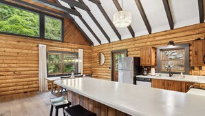 Eine moderne Kücheneinrichtung im Blockhausstil mit einer großen Kochinsel, Holzwänden und großen Fenstern.