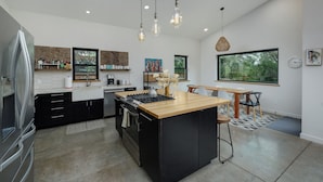 A modern kitchen with a central island, black cabinets, stainless steel appliances, and pendant lighting. - Gallatin River Retreat: 3BR Home with Hot Tub, Fly Fishing & Stunning Views (Gallatin Gateway)