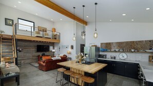 A modern kitchen with a central island, bar stools, and a loft bedroom with a balcony. - Gallatin River Retreat: 3BR Home with Hot Tub, Fly Fishing & Stunning Views (Gallatin Gateway)
