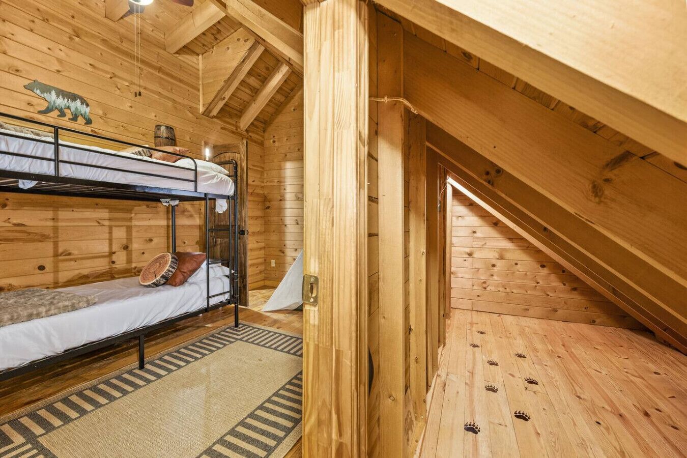 Ein Holzhüttenraum mit Etagenbetten, einem Teppich und einem Holzboden mit Tierpfoten-Motiv.