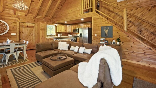 A log cabin interior with a wooden staircase, a dining area, a living room with a sectional sofa, and a kitchen. - HazelBrook Haven- Hot Tub, Firepit, Grill (Hazel Green)