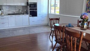 A modern kitchen with white cabinets, a dining table with wooden chairs, and a large window providing natural light. - Westgate Three and one small room house 🏠  (Auckland)
