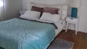 A bedroom with a bed, a nightstand, a lamp, and a painting on the wall. - Westgate Three and one small room house 🏠  (Auckland)