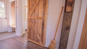 Une porte en bois avec un balai appuyé contre, un mur blanc et un plancher en bois.