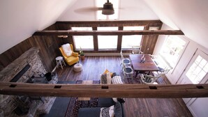 Un espace de vie de style industriel, avec un plafond haut, des poutres apparentes en bois, un coin repas comprenant une table et des chaises, et un coin salon confortable avec un canapé et des fauteuils.