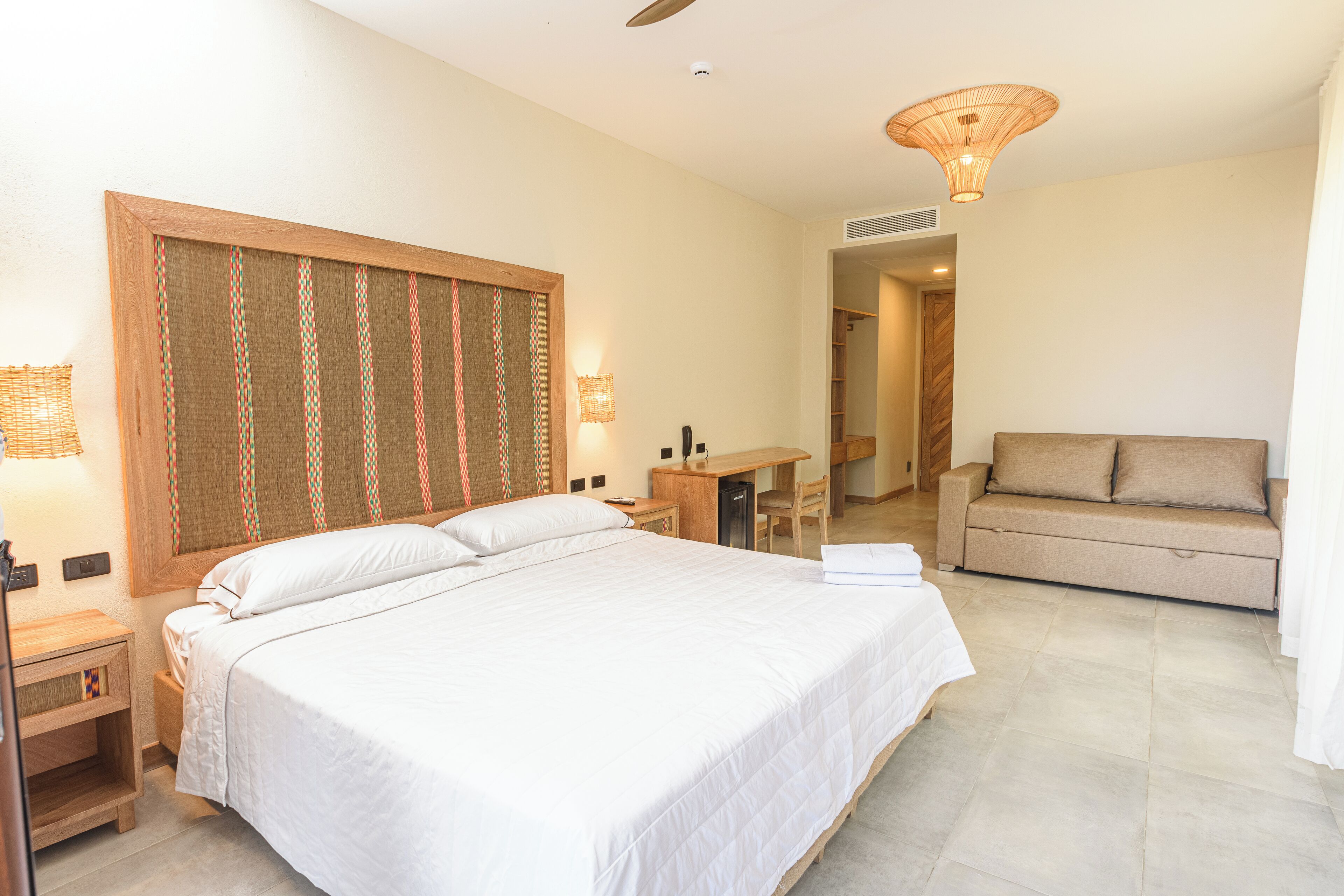 A bedroom with a large bed, a desk, a sofa, and a ceiling fan.