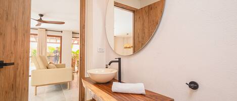 Ein Badezimmer mit einem Holzkosmetikschrank, einem runden Spiegel und einem beige farbenen Waschbecken.