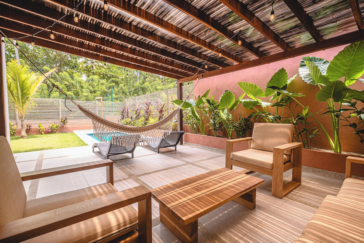 Une terrasse extérieure avec des meubles en bois, un hamac et de grandes plantes.