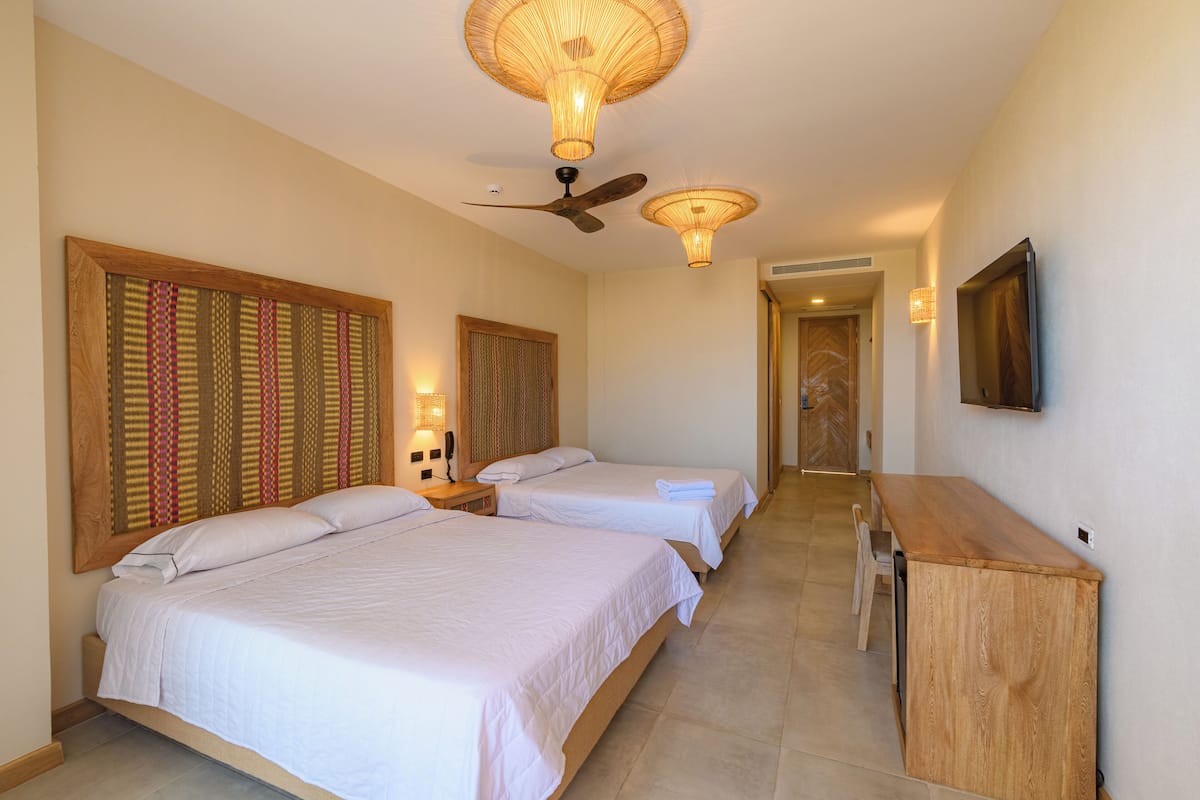 Une chambre d’hôtel avec deux lits, un ventilateur de plafond et un bureau en bois.