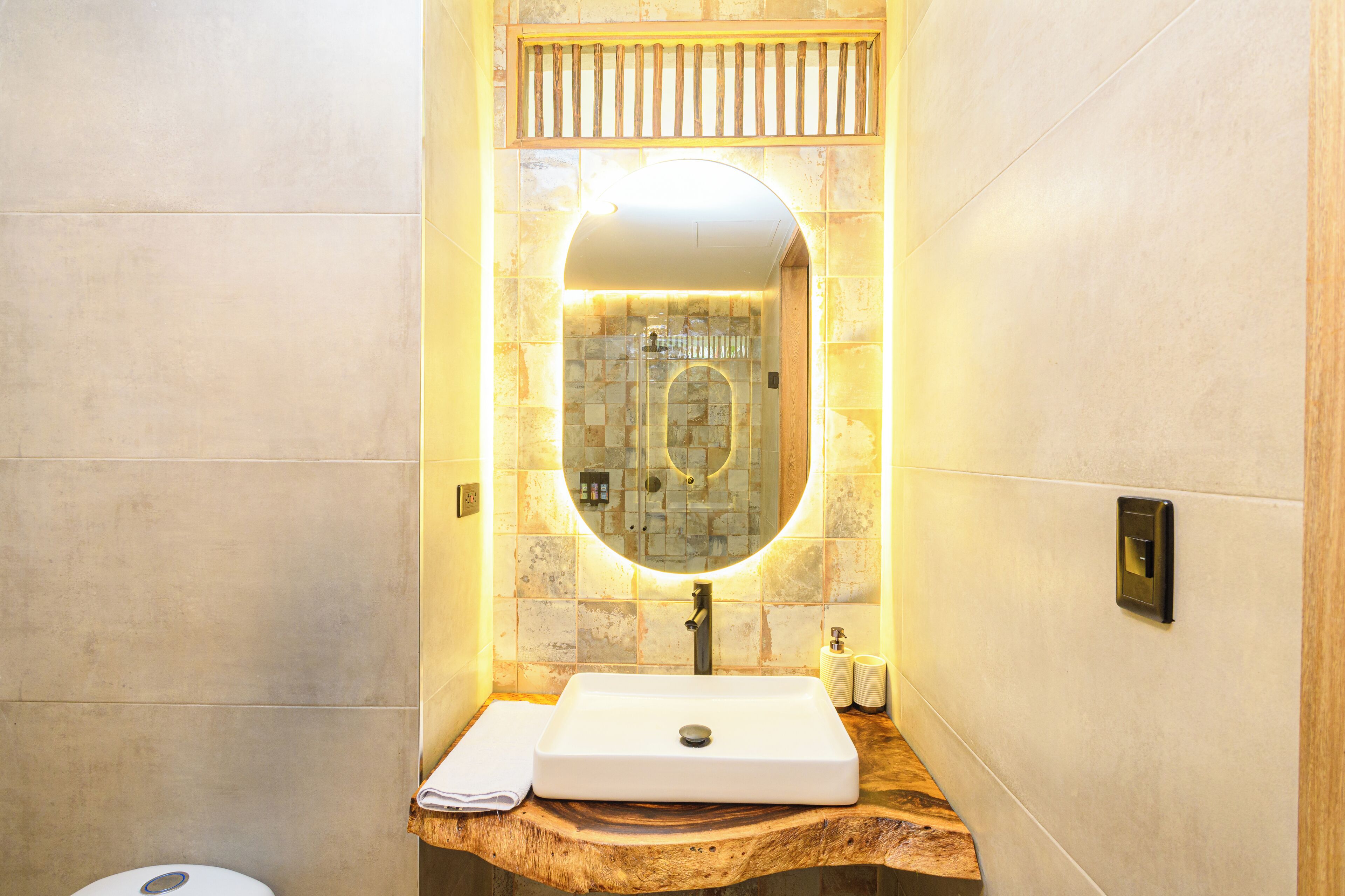 Un baño con tocador de madera, un lavamanos blanco y un espejo con luz superior.