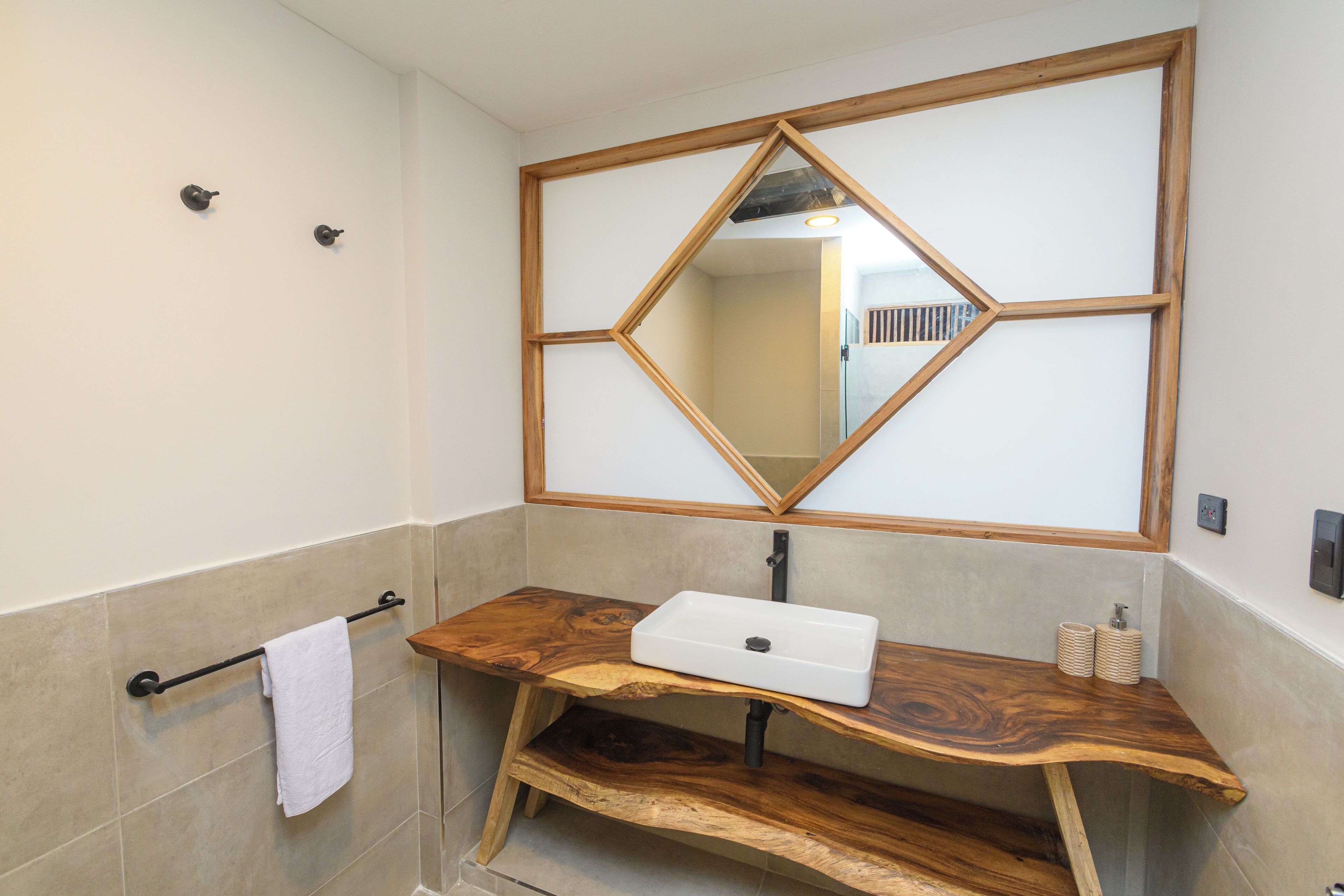 A bathroom with a wooden vanity, a white sink, and a diamond-shaped mirror.