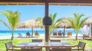Un restaurant situé en bord de mer, avec des tables et des chaises, des palmiers et une vue sur l’océan.