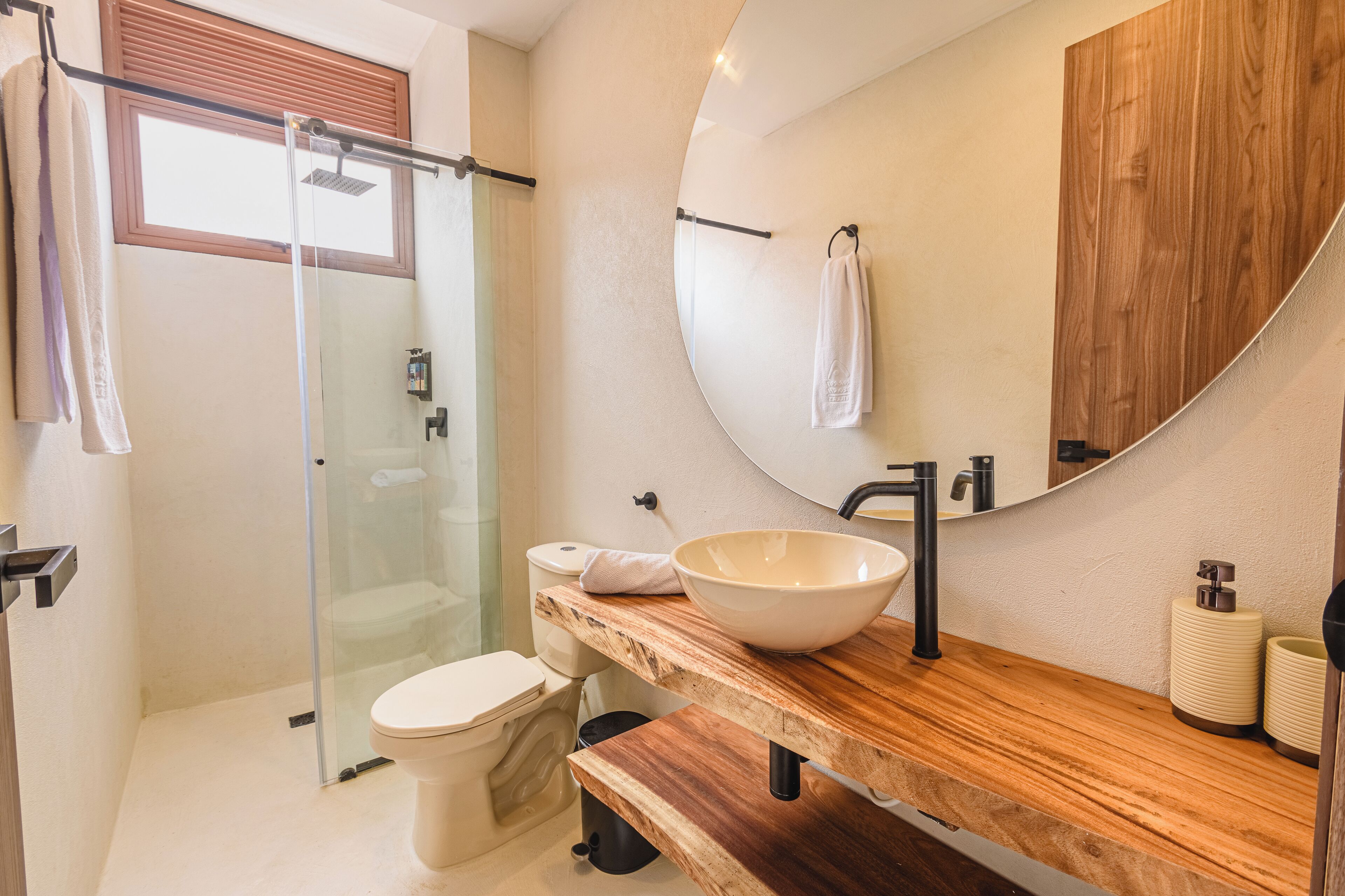 Un baño moderno con cabina de ducha de vidrio, tocador de madera, un espejo grande y un inodoro.