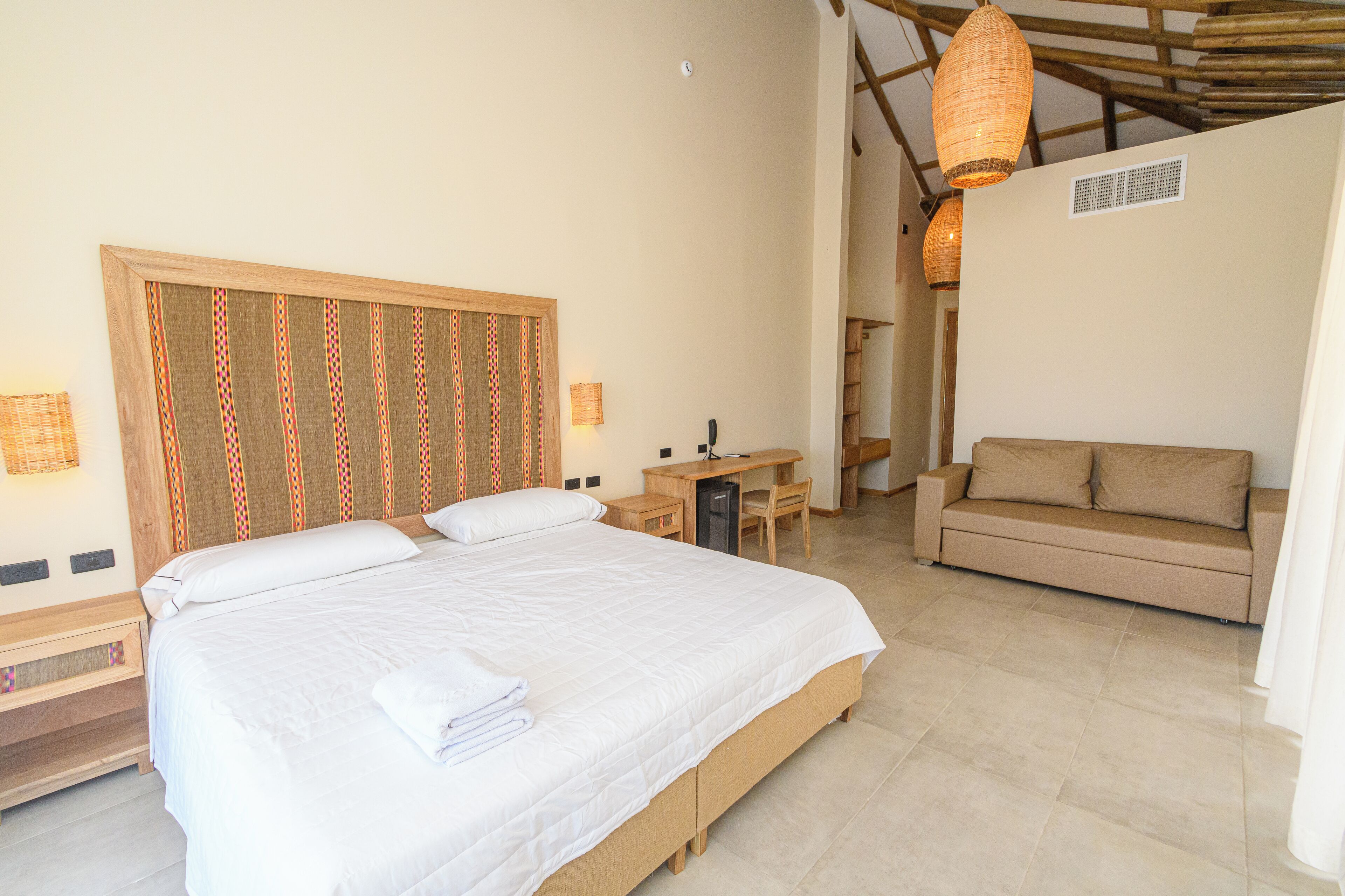 A bedroom with a large bed, a desk, a sofa, and a hanging light fixture.