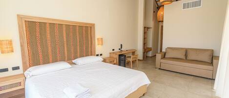 A bedroom with a large bed, a desk, a sofa, and a hanging light fixture.