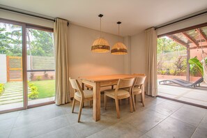 A dining area with a wooden table and chairs, two hanging pendant lights, and a view of a garden through large sliding glass doors. - Senda Kokkos Beach (Santa Marta)