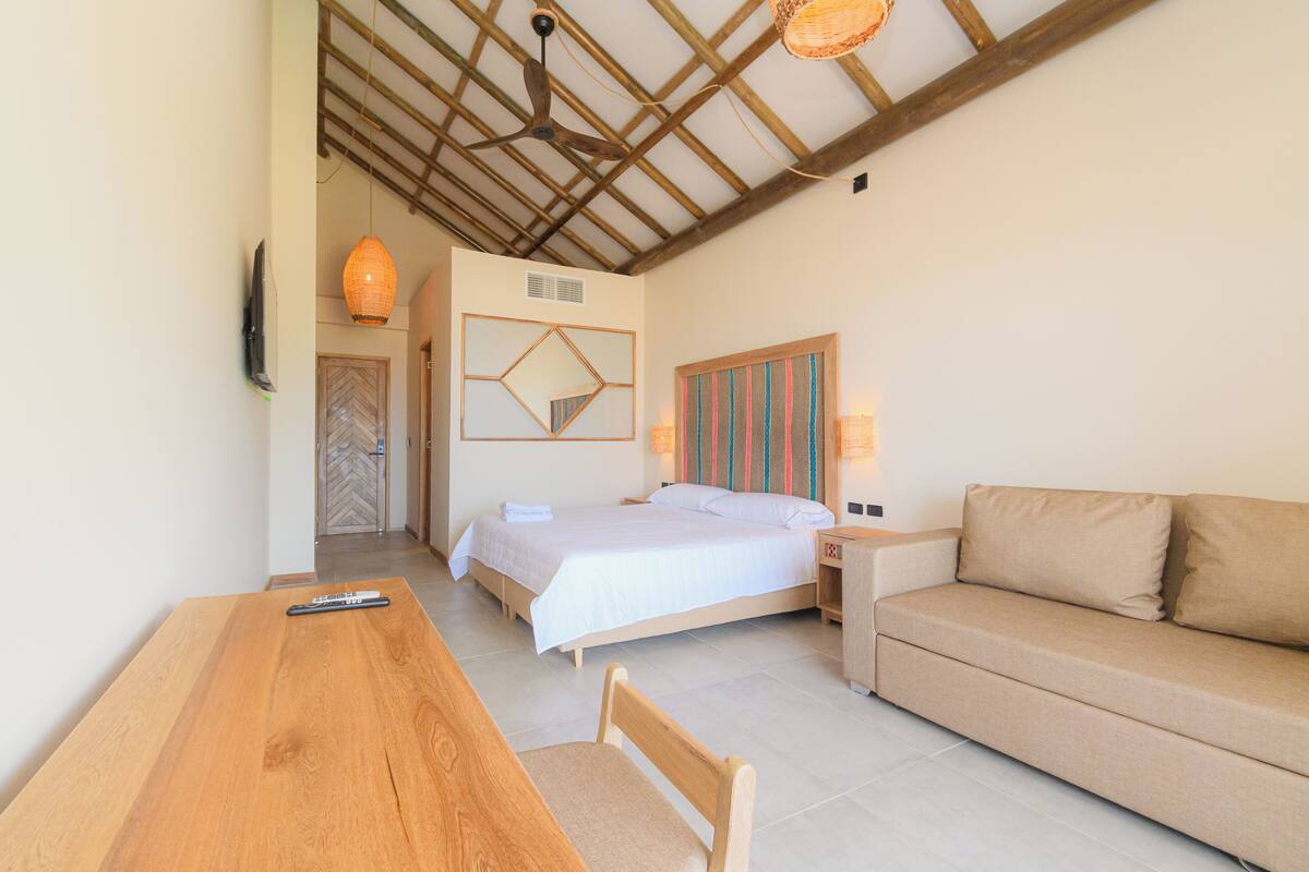 Une chambre à coucher avec un lit, une table en bois, un canapé, une télévision et un ventilateur de plafond.