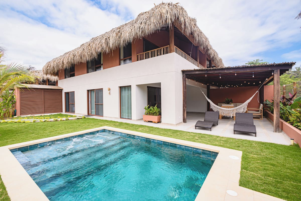 Une maison moderne dotée d’une piscine, d’un hamac et d’un toit de chaume.