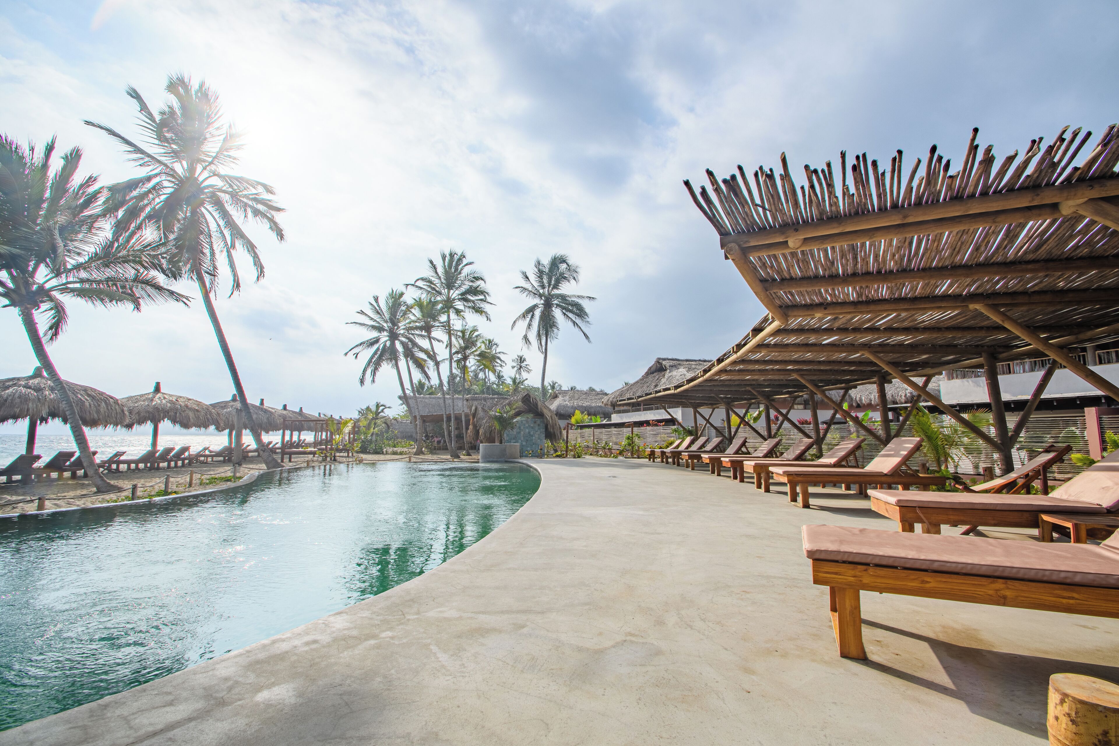 A poolside area with lounge chairs and thatched umbrellas, surrounded by palm trees.