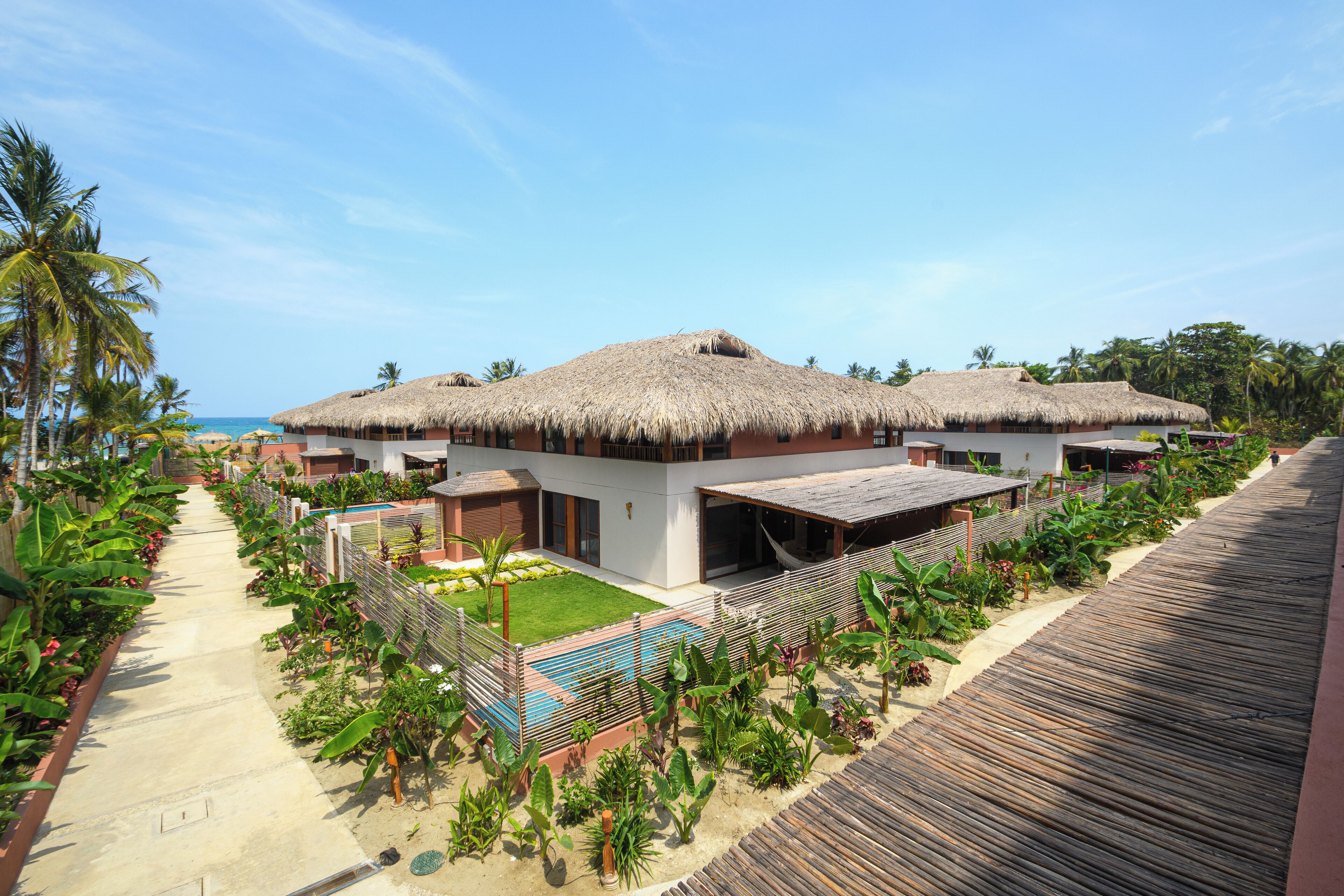 A resort with thatched-roof buildings, a pool, and a wooden walkway.