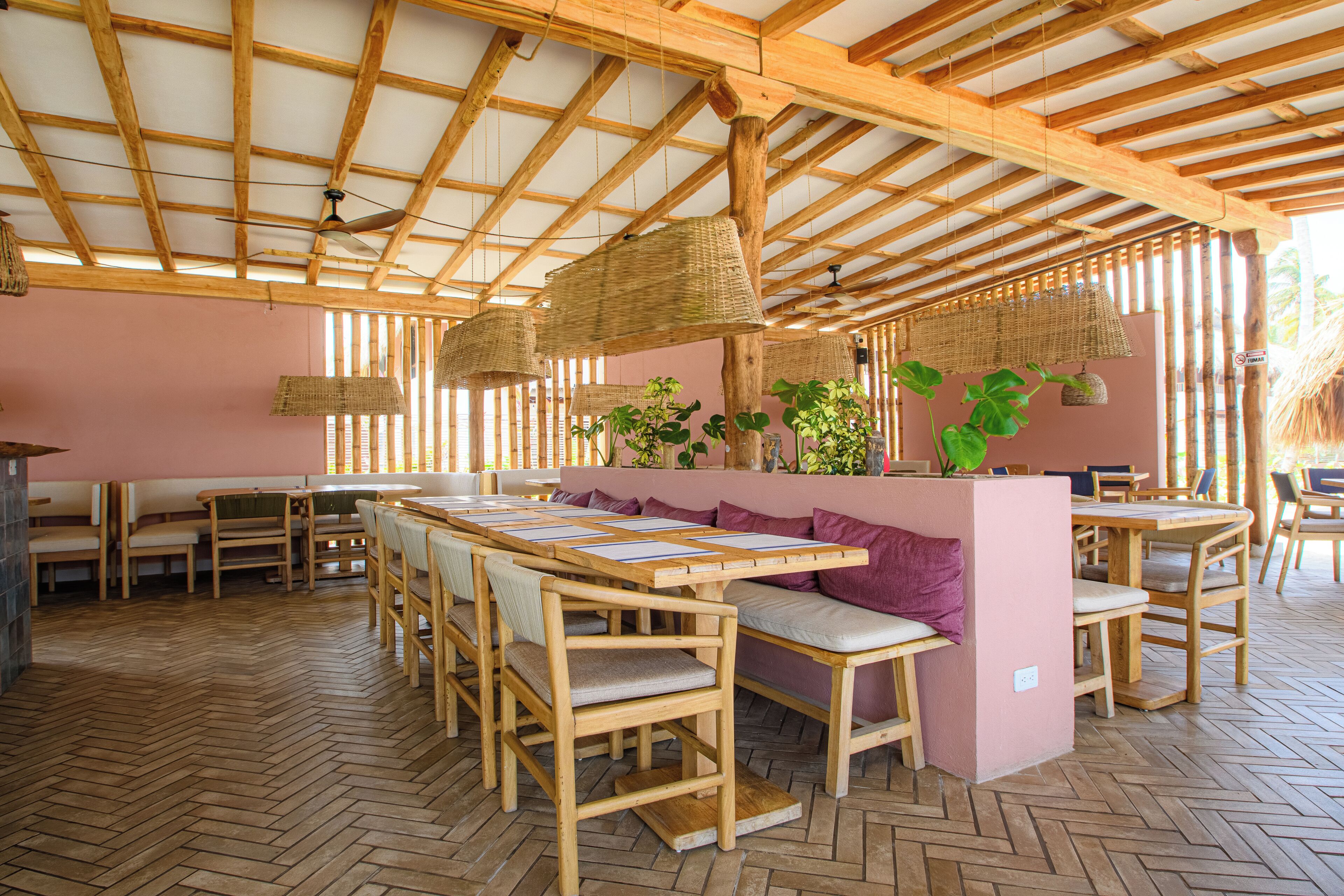 A restaurant with wooden tables and benches, a herringbone floor, and a bamboo ceiling.