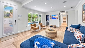 Un salon spacieux avec un canapé bleu, un pouf rond et un coin repas doté de chaises en bois.