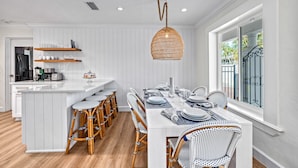 Une cuisine moderne avec des meubles blancs, un îlot central doté de tabourets et un luminaire suspendu.