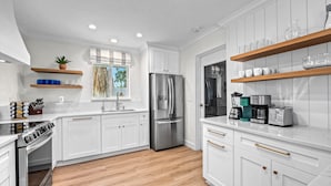 Une cuisine moderne avec des meubles blancs, des appareils en acier inoxydable et un plancher en bois.