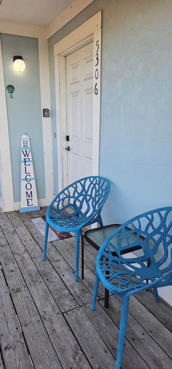 Un portico in legno con due sedie blu, una porta bianca con il numero 5306 e un cartello con la scritta 'WELCOME'.