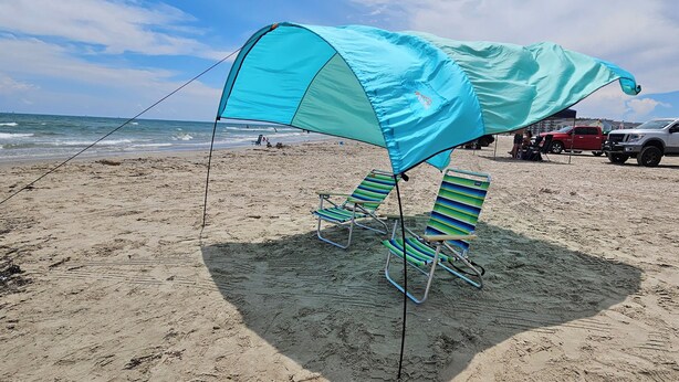 Une plage avec un parasol bleu et des chaises de plage à rayures.